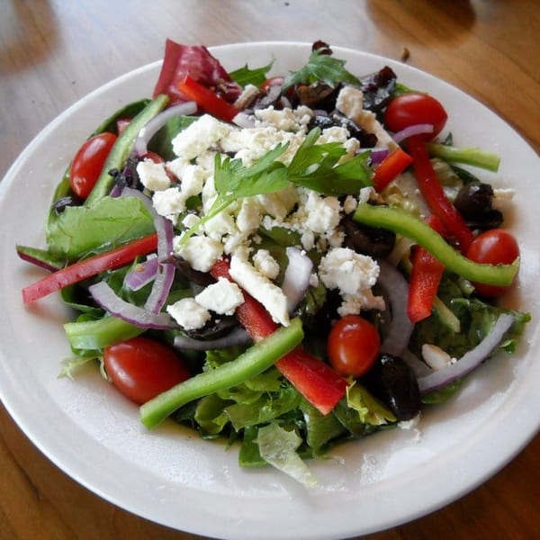 A vibrant Greek salad with feta, olives, tomatoes, and peppers on a white plate at Greg's Grill.