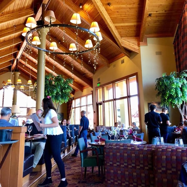 The spacious dining room at Greg's Grill, featuring a high wooden ceiling, large windows, and elegant lighting.