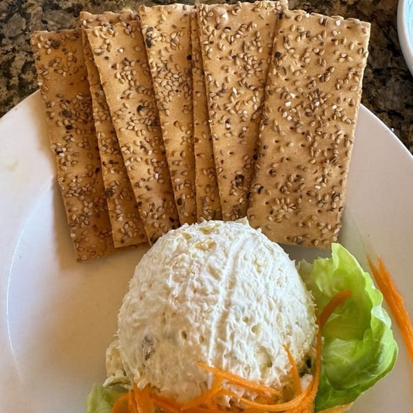 A scoop of chicken salad with lettuce, shredded carrots, and sesame seed crackers on a white plate.