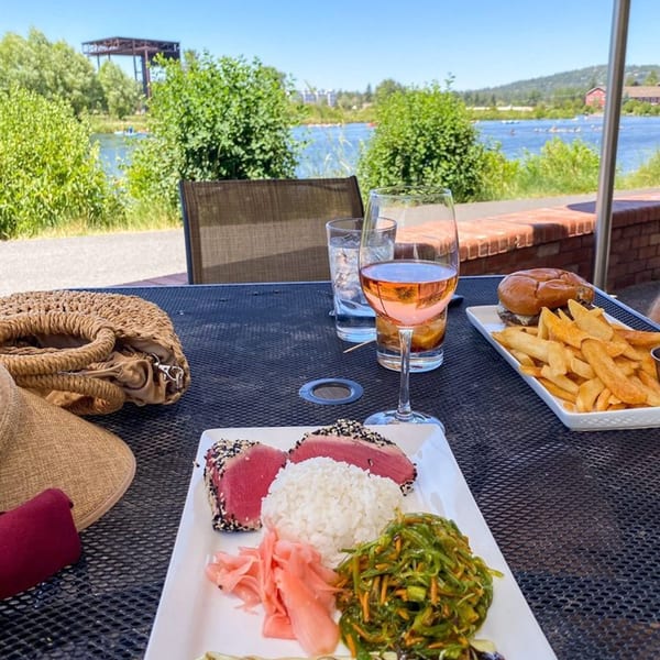 Seared tuna, rice, seaweed salad, and pickled ginger on an outdoor patio overlooking a river.