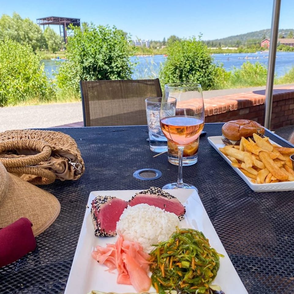 Seared tuna, rice, seaweed salad, and pickled ginger on an outdoor patio overlooking a river.