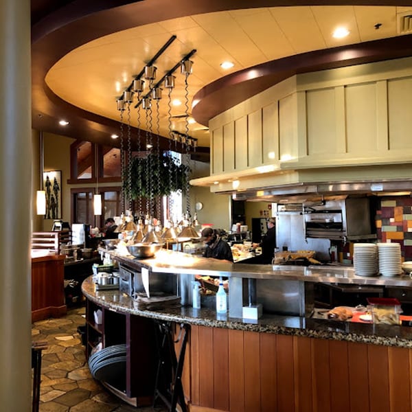 The open kitchen at Greg's Grill steakhouse, with chefs working behind a granite counter and warm lighting.