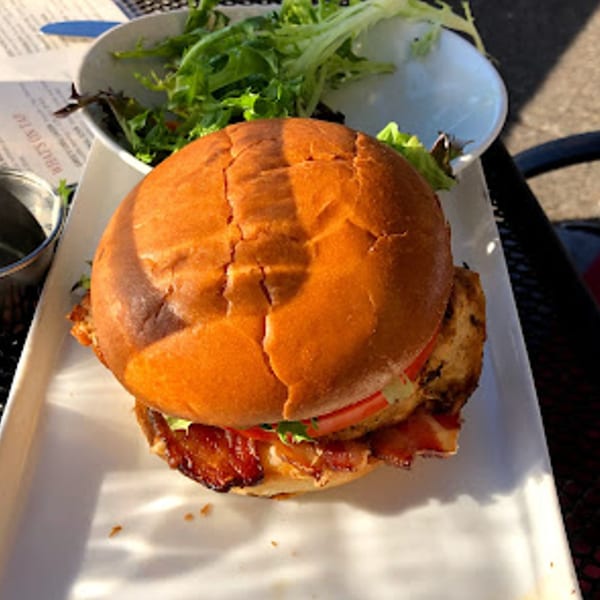 A chicken sandwich with bacon, lettuce, and tomato, served with a side salad at Greg's Grill.