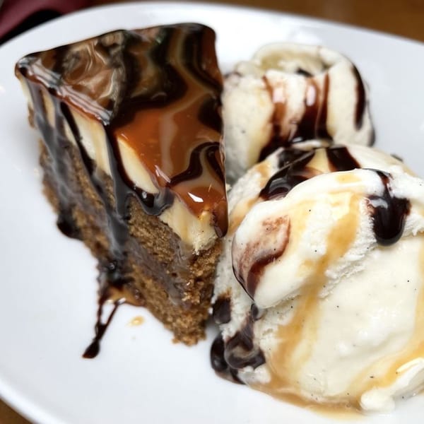 A slice of chocolate and caramel cake with three scoops of vanilla ice cream on a white plate.