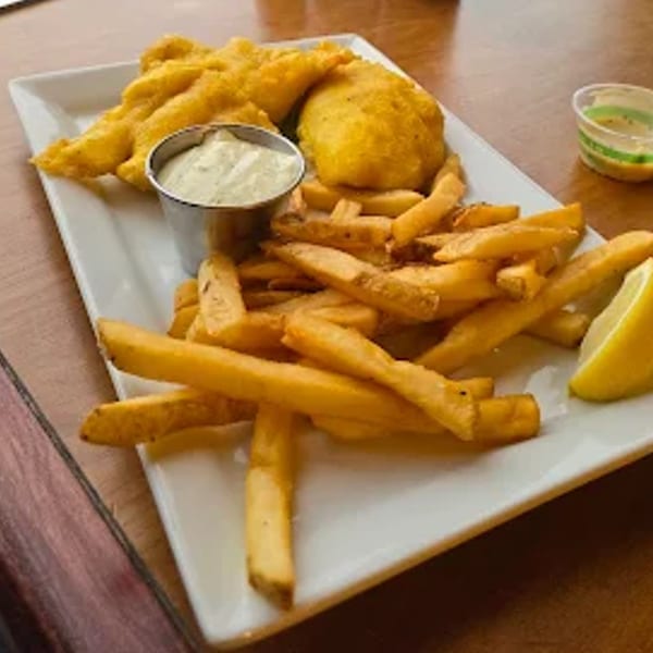 Crispy fish and chips with tartar sauce and a lemon wedge on a white rectangular plate.